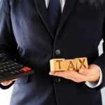 What Is a 1031 Exchange? We see here a professional holding a big calculator and cudes that read TAX